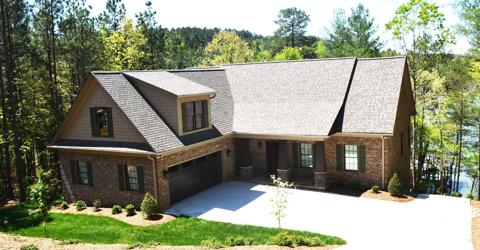 A large brick house is surrounded by trees and a lake