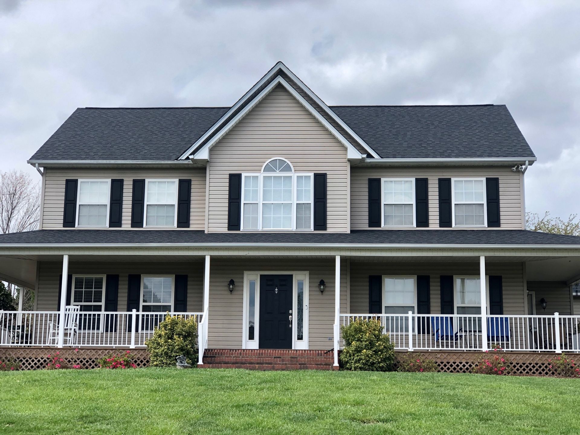 A large house with a porch and black shutters on a cloudy day.