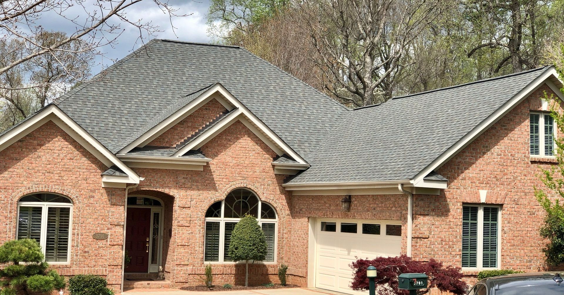A large brick house with a gray roof and a car parked in front of it.