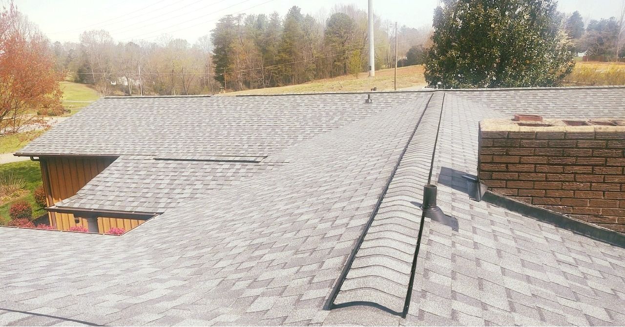 A roof with a chimney and a tree in the background.