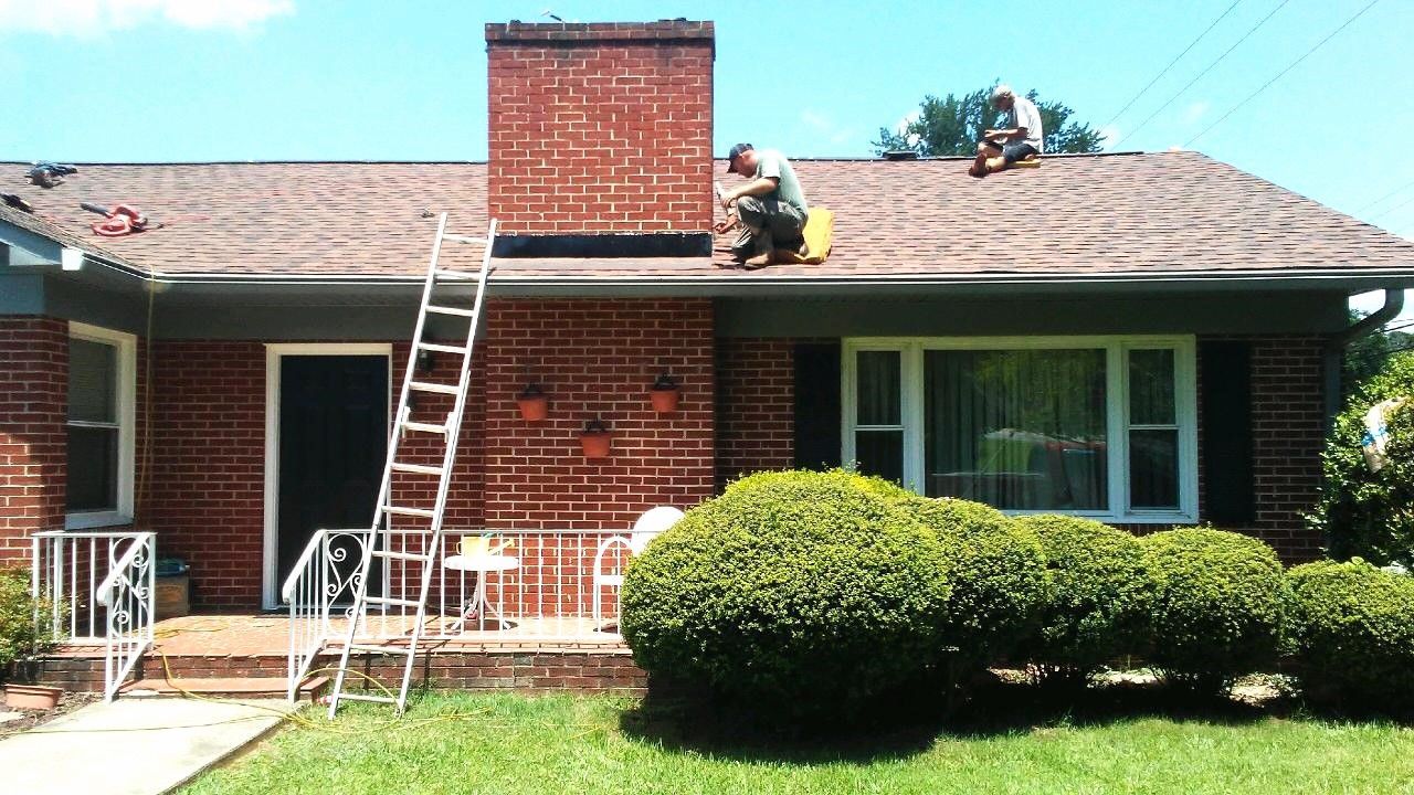 Two men are working on the roof of a brick house
