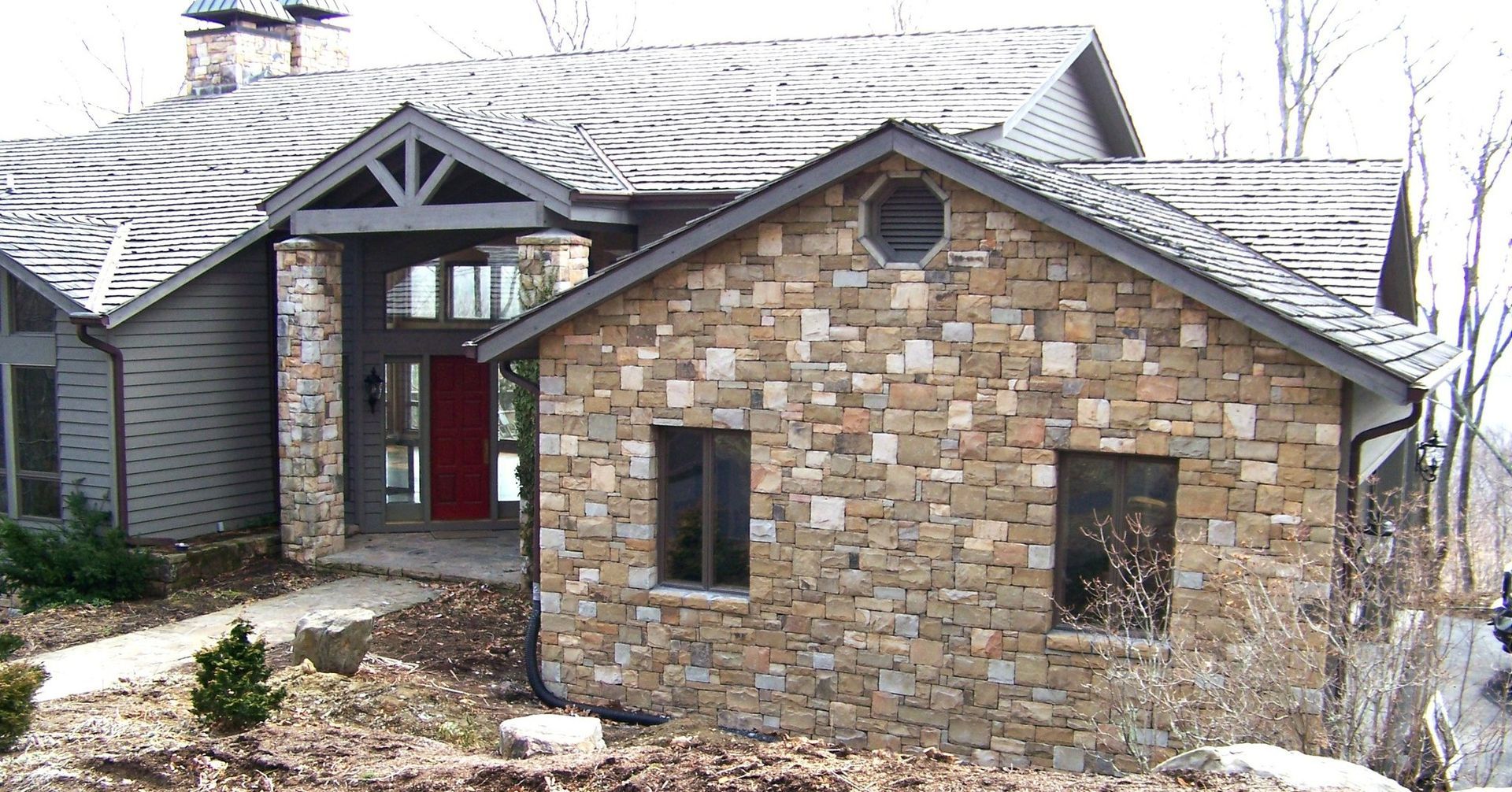 A large stone house with a gray roof and a red door
