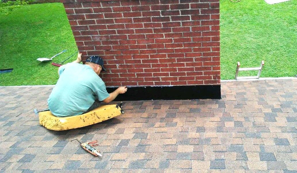 A man is kneeling on the ground painting a brick wall
