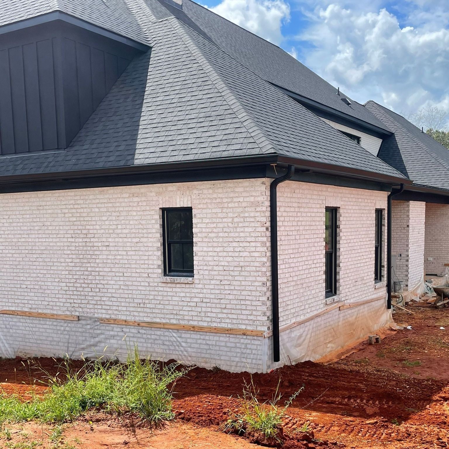 A white brick house with a black roof is being built.