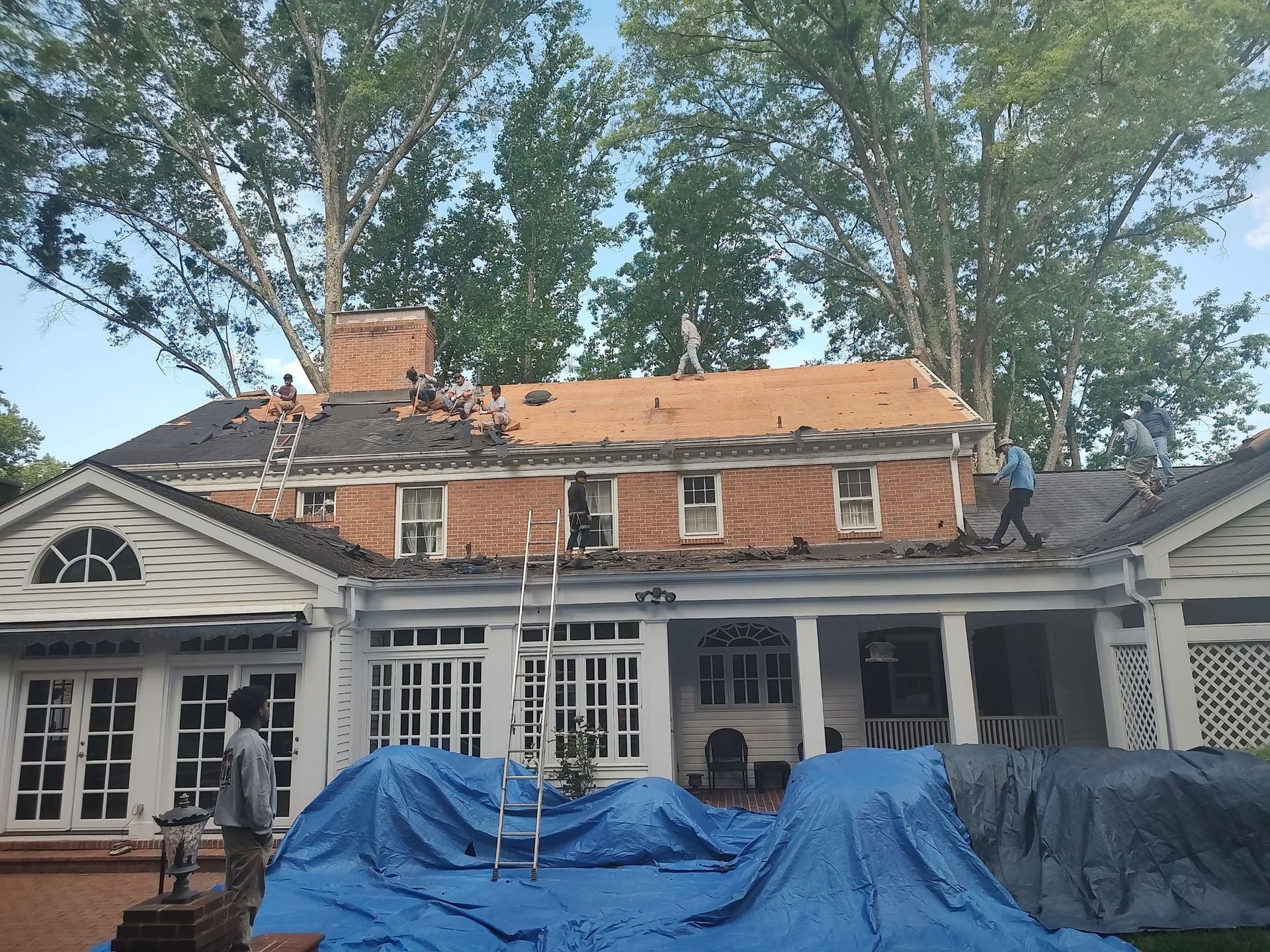 A group of people are working on the roof of a large brick house.