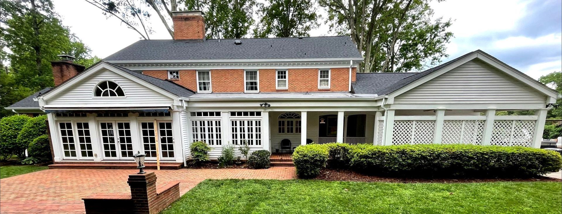 A large brick house with a gray roof and white trim is sitting on top of a lush green lawn.