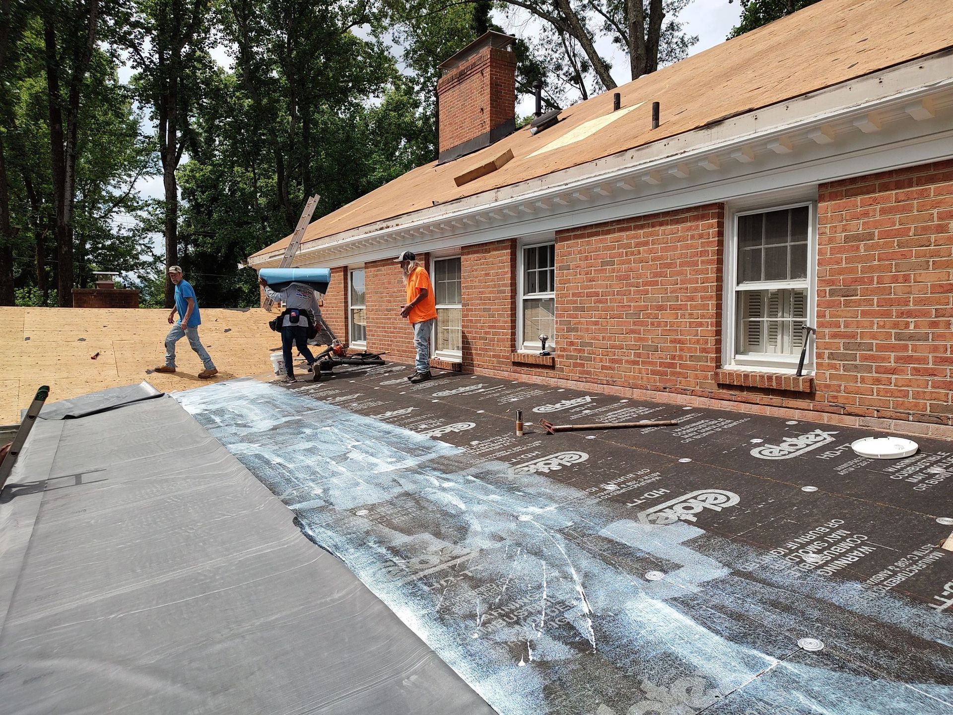A group of men are working on a roof of a brick house.