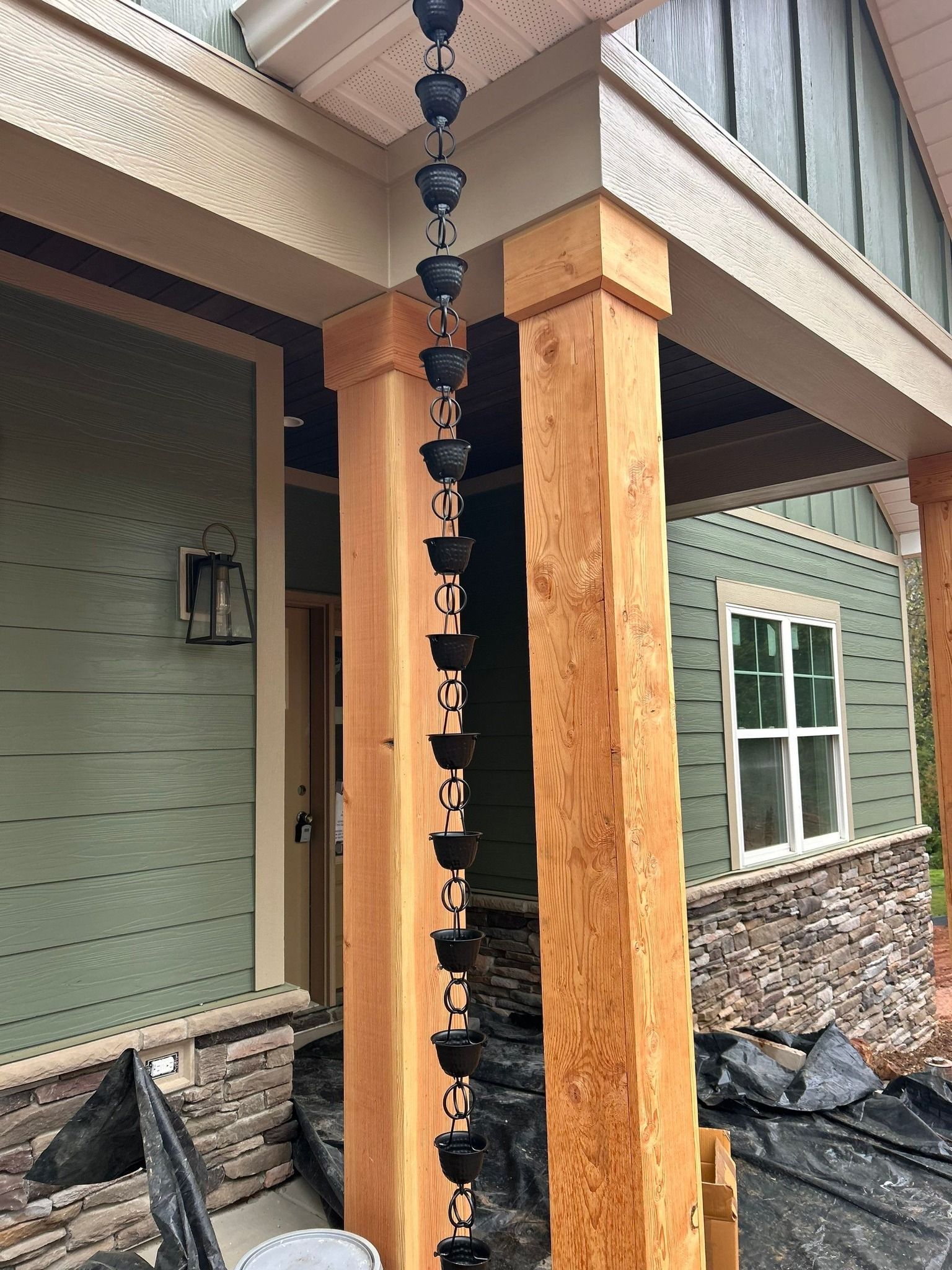 A rain chain is hanging from a wooden post on a porch.