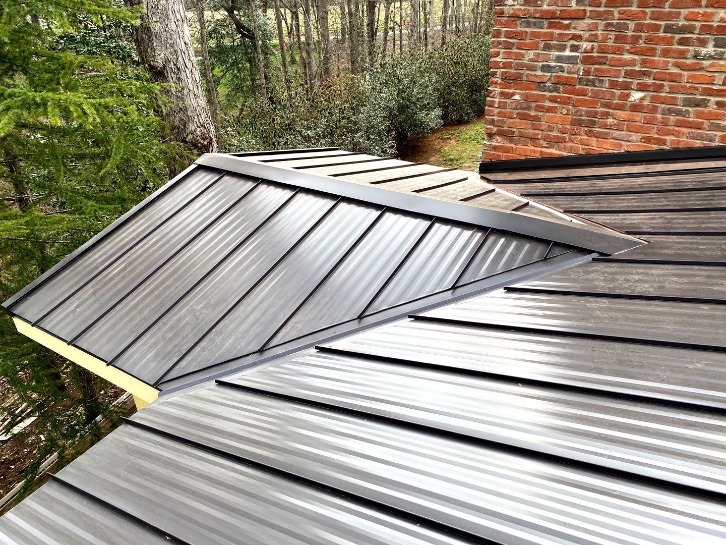A close up of a metal roof with a brick chimney in the background.