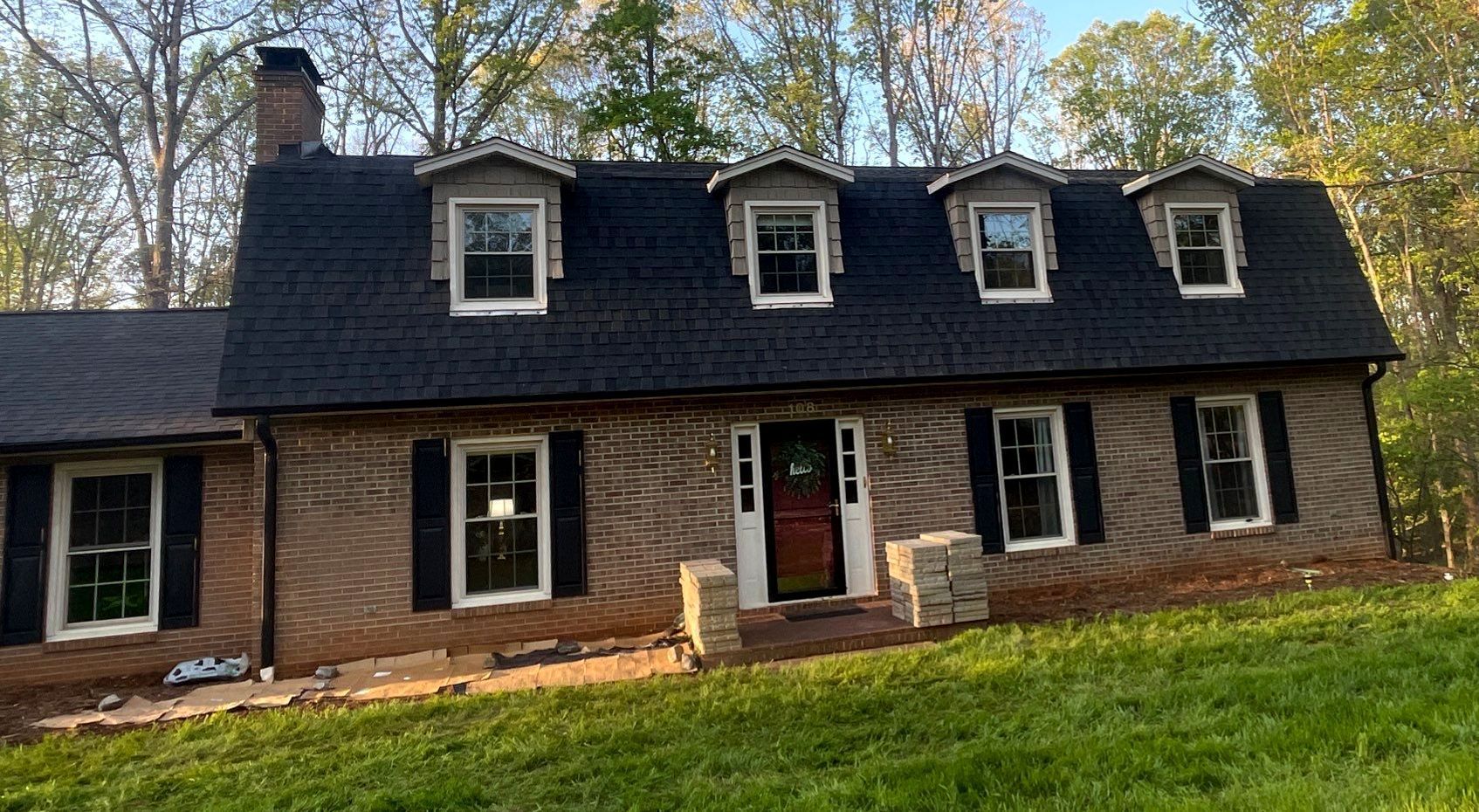 A large brick house with a black roof and white shutters is sitting on top of a lush green field.