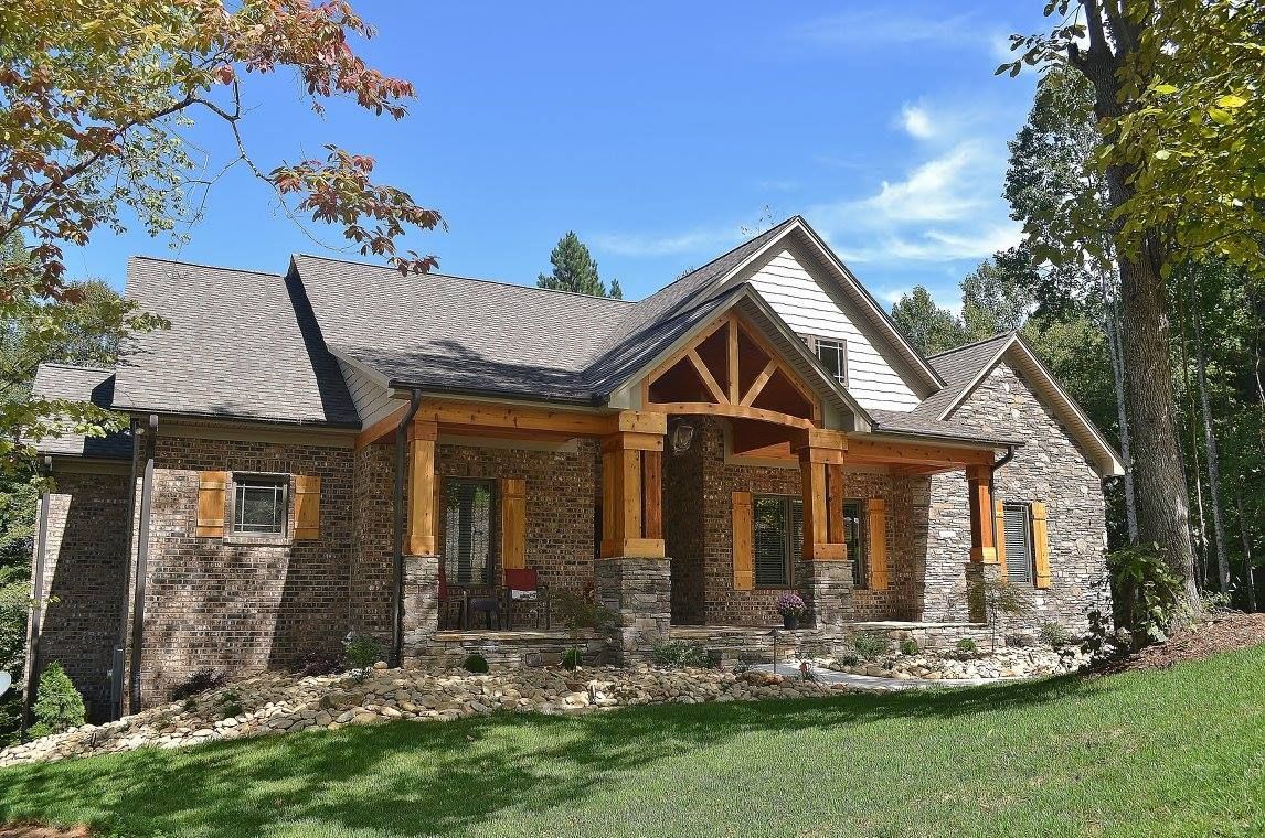 A large stone house with a wooden porch is sitting on top of a lush green hill.