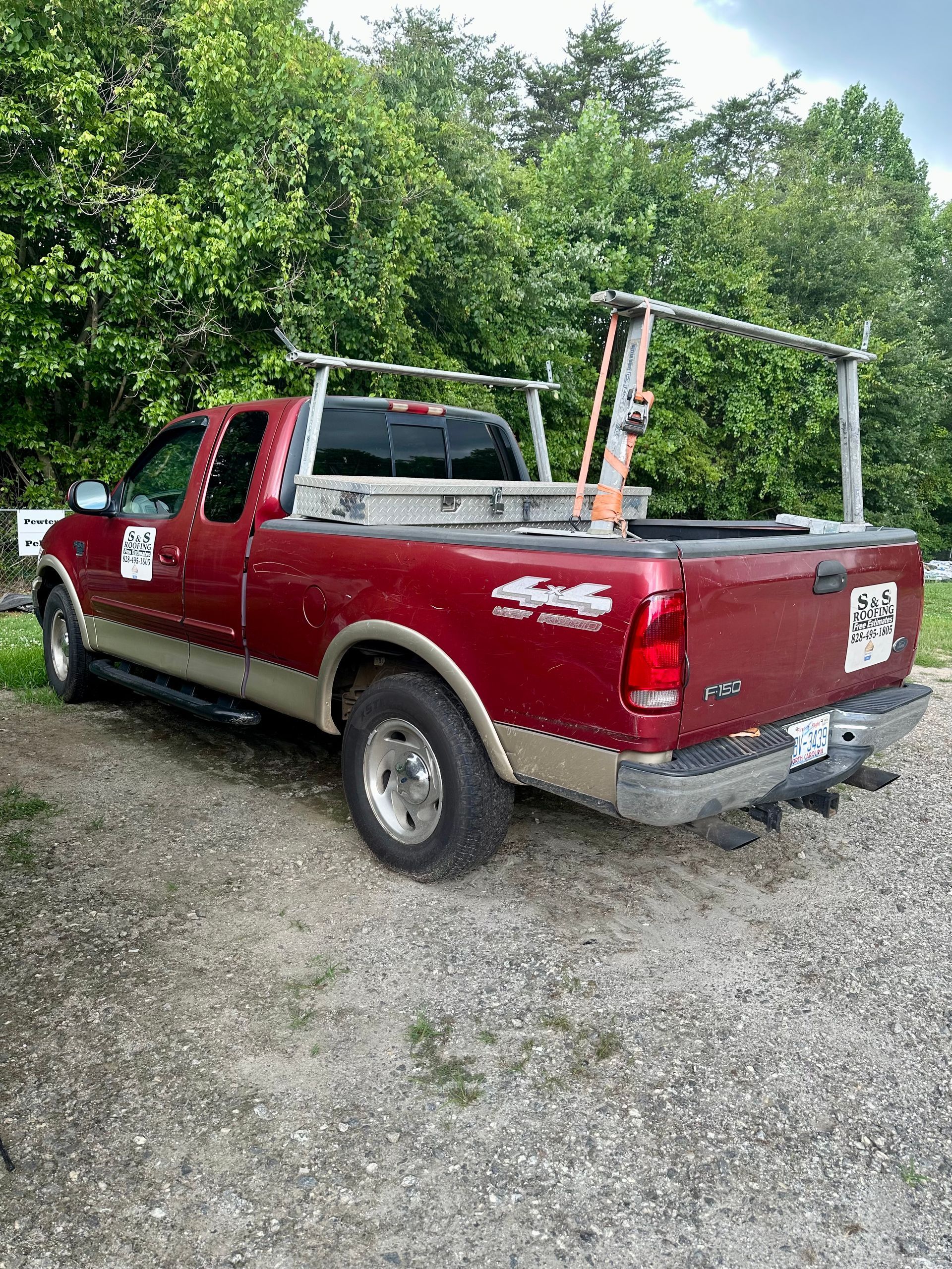 A red truck with a ladder rack on the back is parked in a gravel lot.