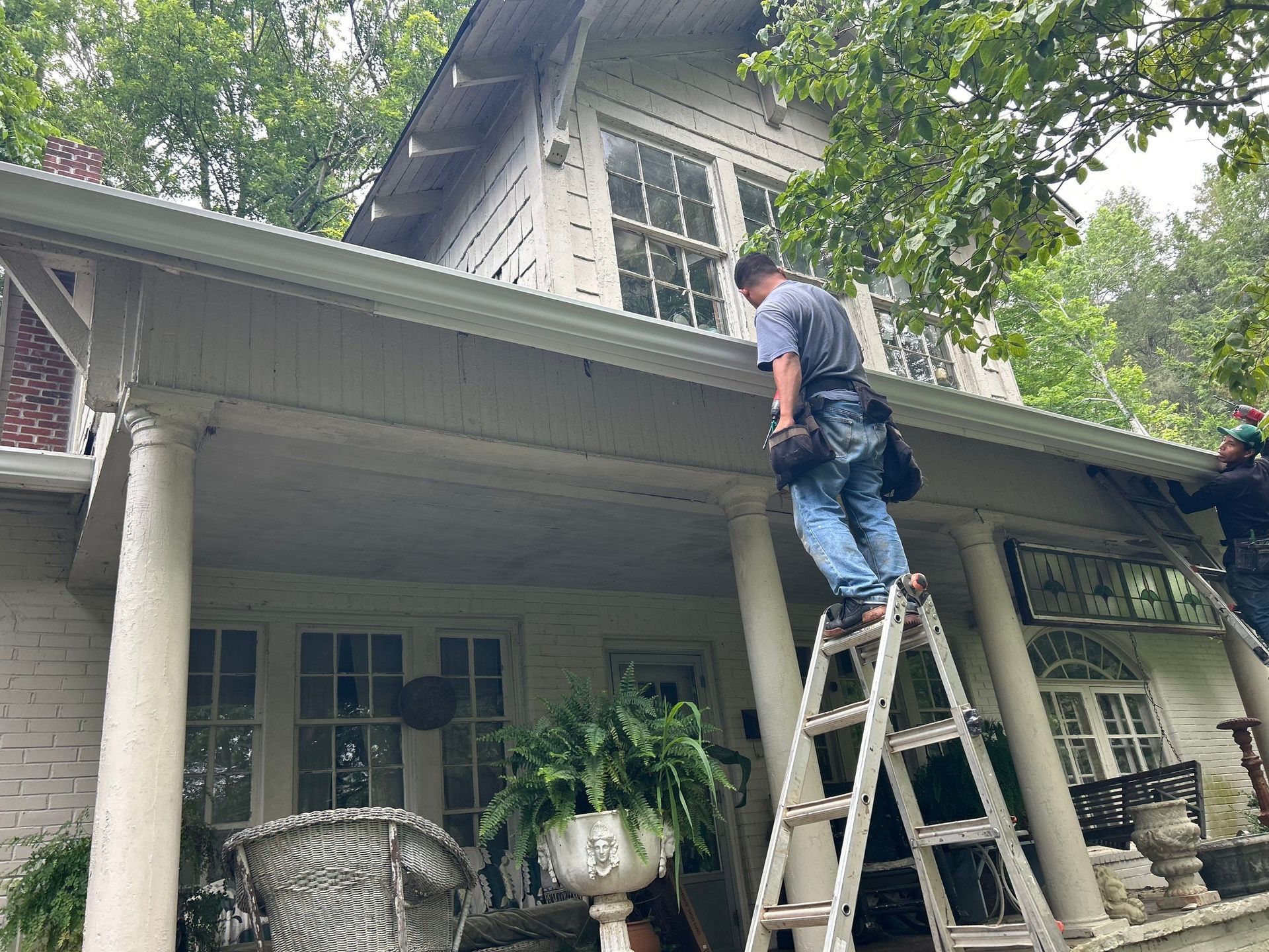 A man is standing on a ladder on the roof of a house.