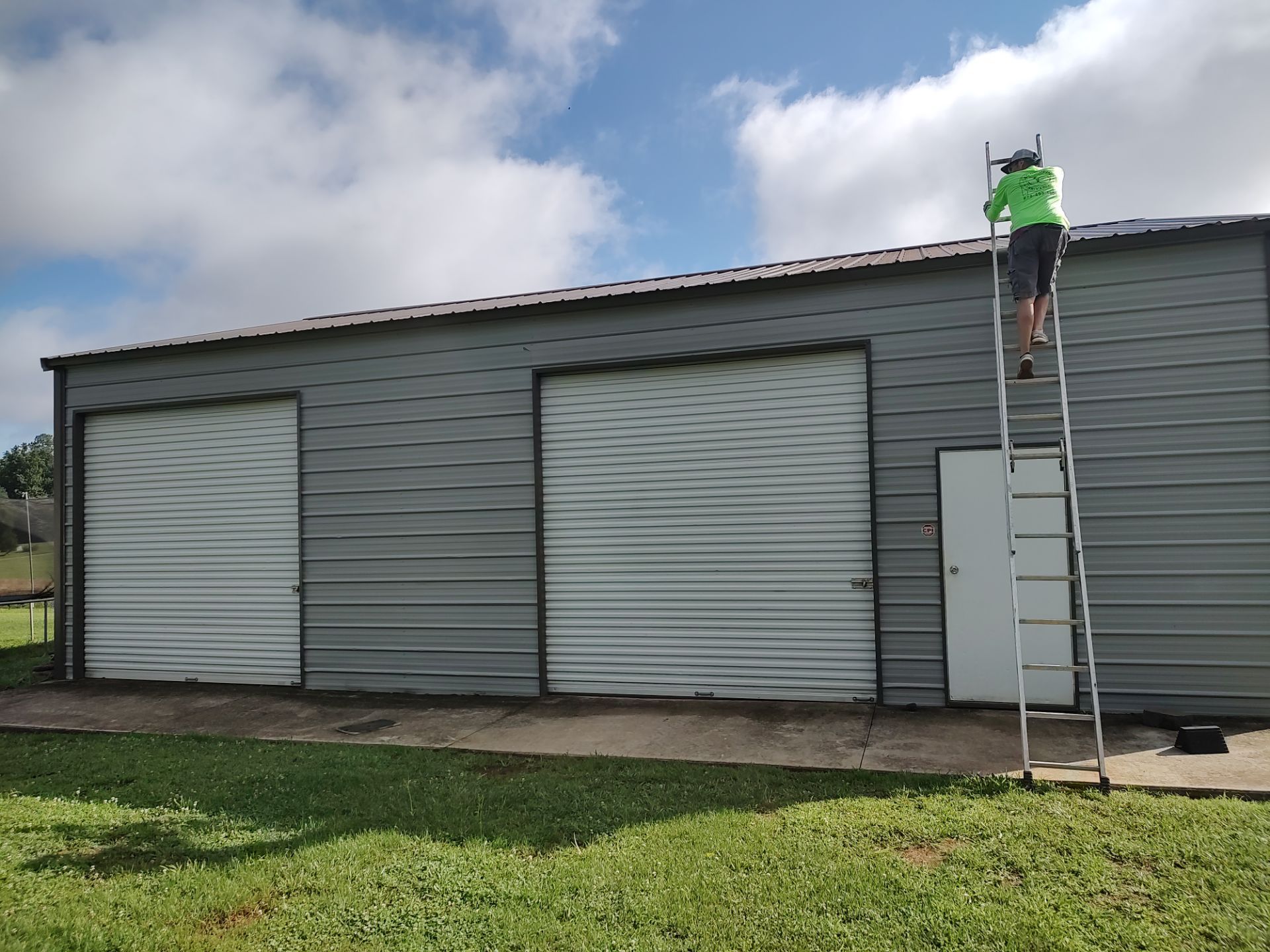 A man is standing on a ladder painting the side of a building.