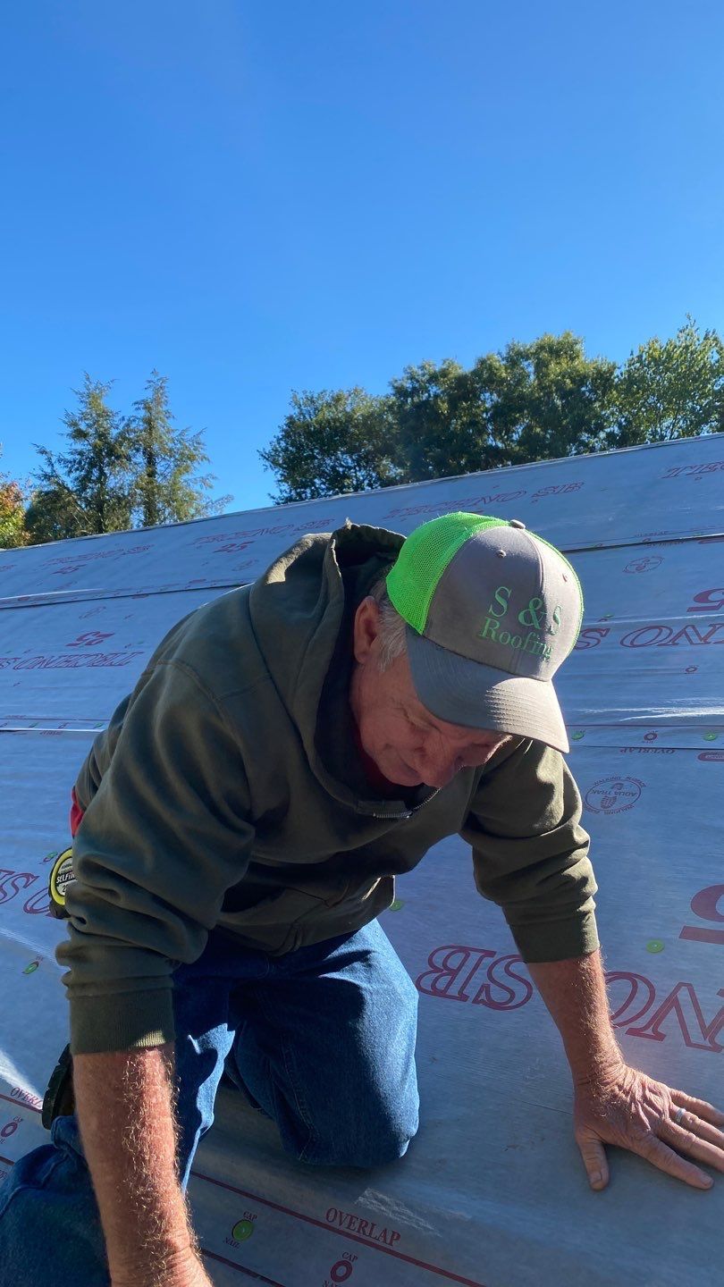 A man wearing a hat is kneeling down on a roof.
