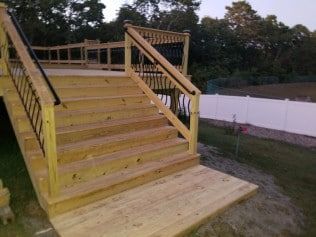 A wooden deck with stairs leading up to it and a white fence in the background.