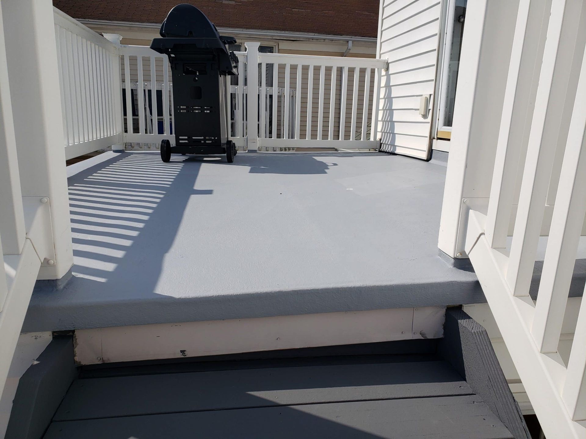 A skateboard is sitting on a deck next to a grill.