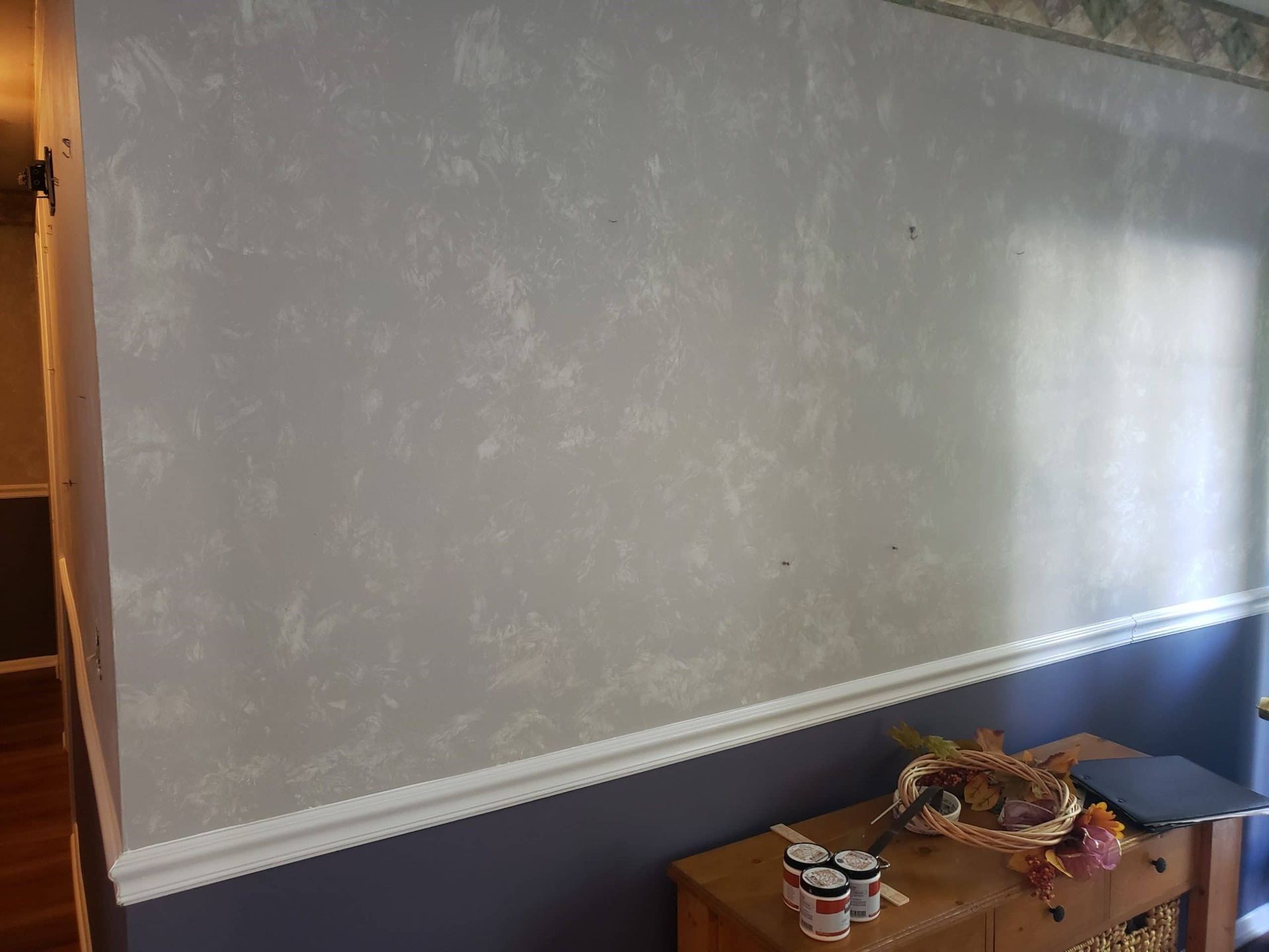 A room with a large wall and a dresser with a basket on it.