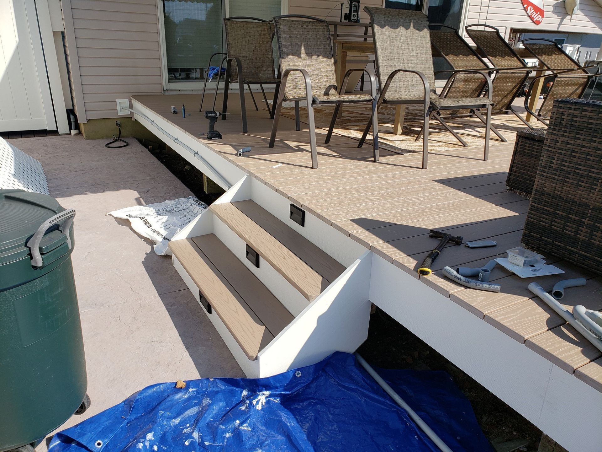 A deck with stairs and chairs and a blue tarp on the ground.
