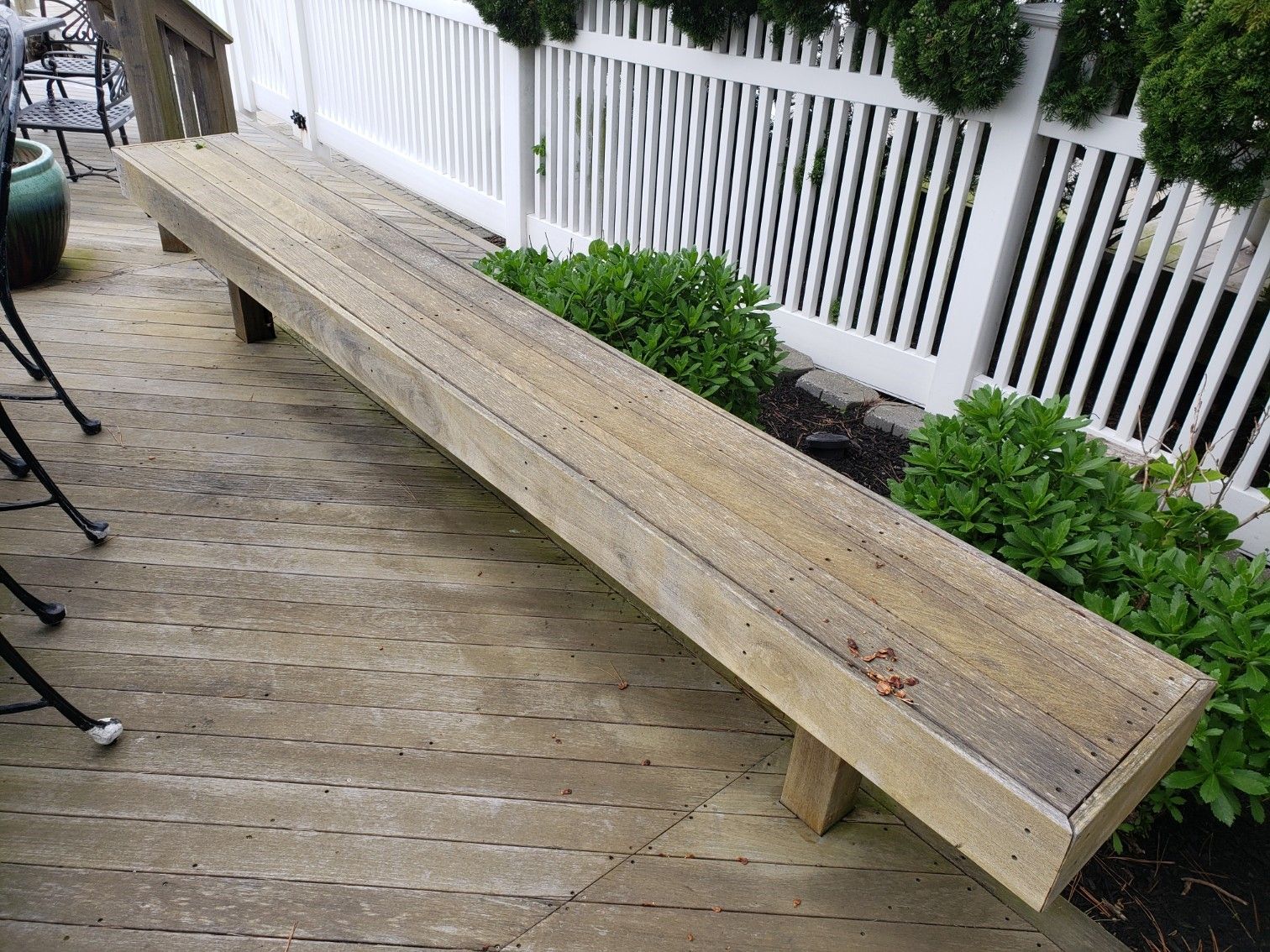 A wooden bench is sitting on a deck next to a white fence.