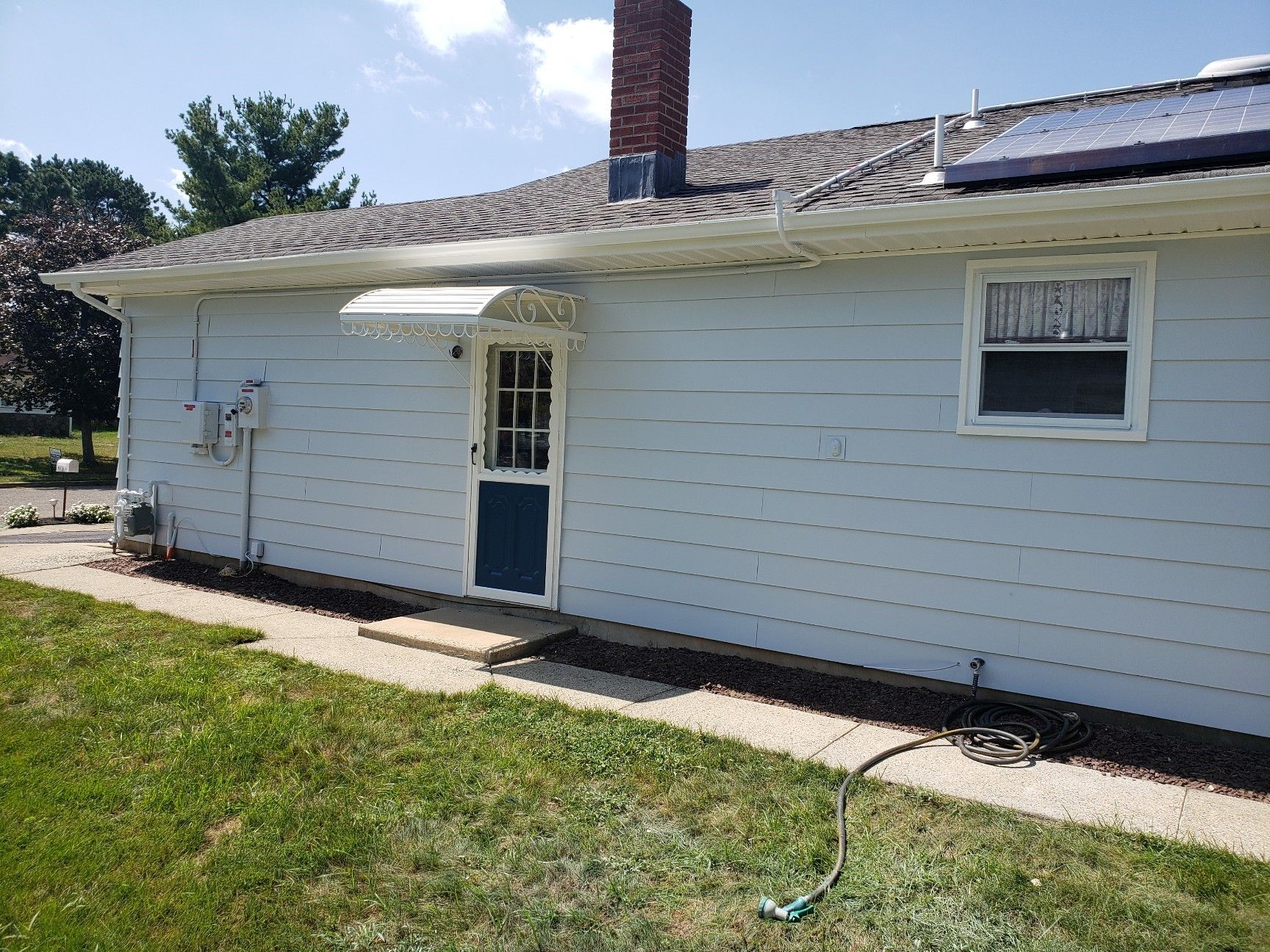 A white house with a blue door and a solar panel on the roof.