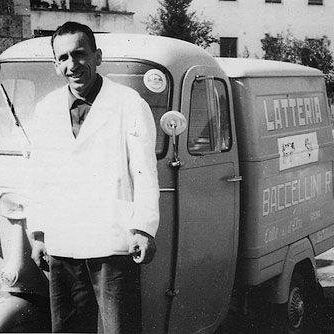 Un uomo in camice bianco è in piedi accanto a un veicolo a tre ruote per la consegna del latte. Sul veicolo c'è scritto