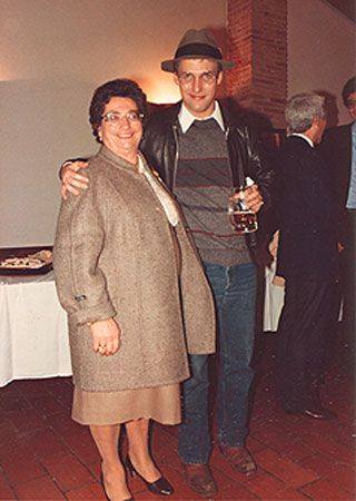 Donna con cappotto e uomo con birra, braccio intorno a lei, in casa.