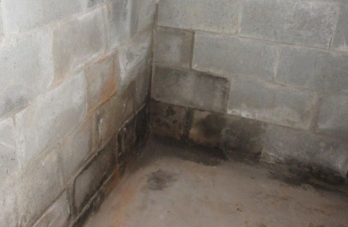 A corner of a basement with a brick wall and a concrete floor.