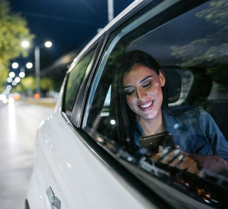 Woman smiling at a phone in the backseat of a white car at night