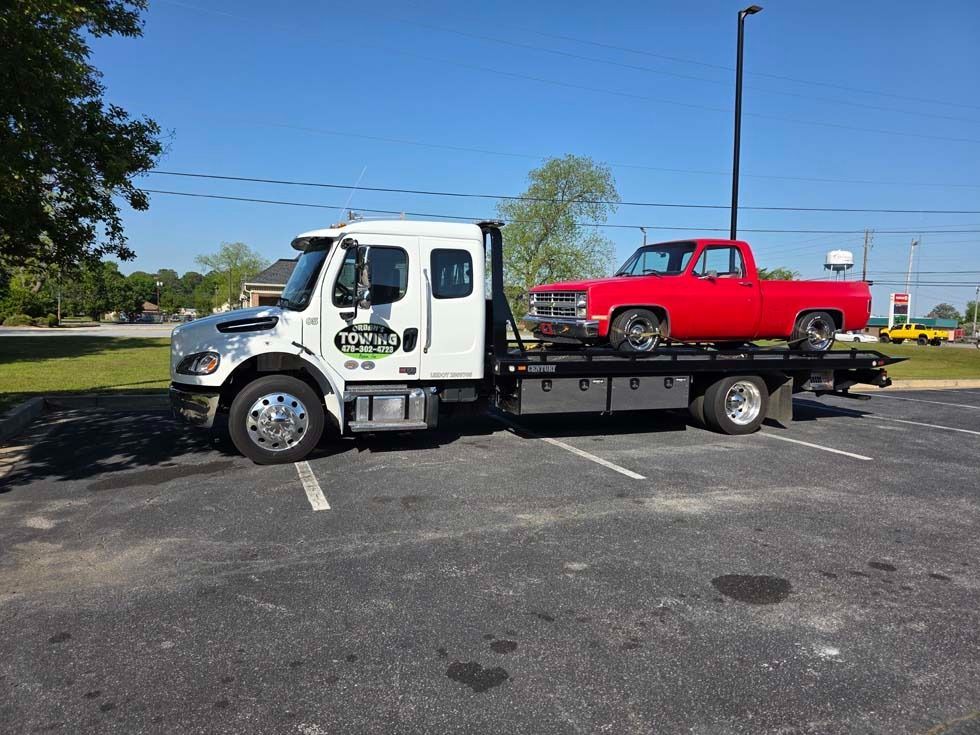 Tow truck transporting a red pickup truck on a sunny day.