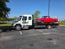 Tow truck transporting a red pickup truck on a sunny day.