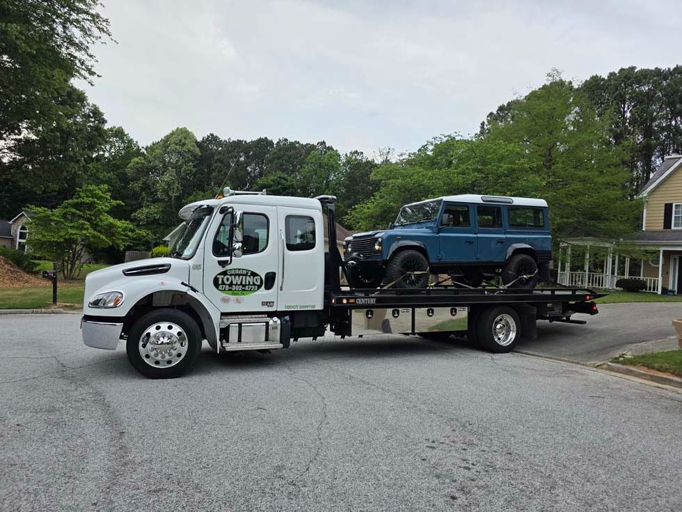 Tow truck carrying a blue SUV on a residential street.
