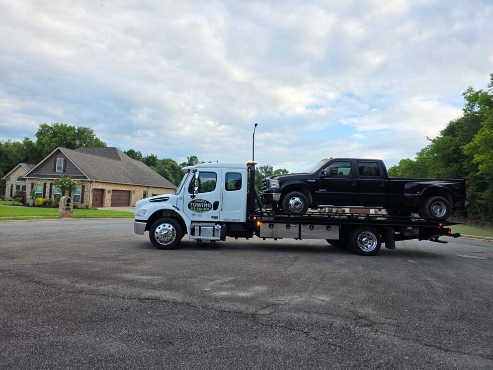 A tow truck with a black pickup truck on its flatbed, parked in front of a house.