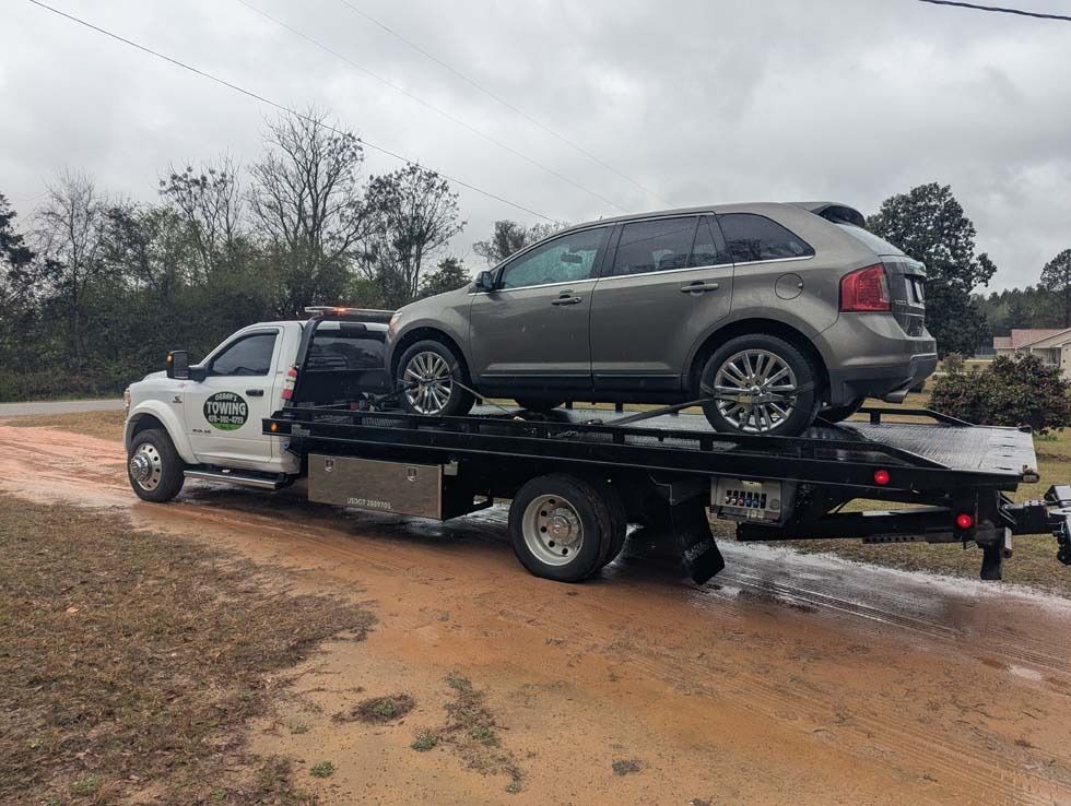 Tow truck carrying a gray SUV on a muddy roadside.