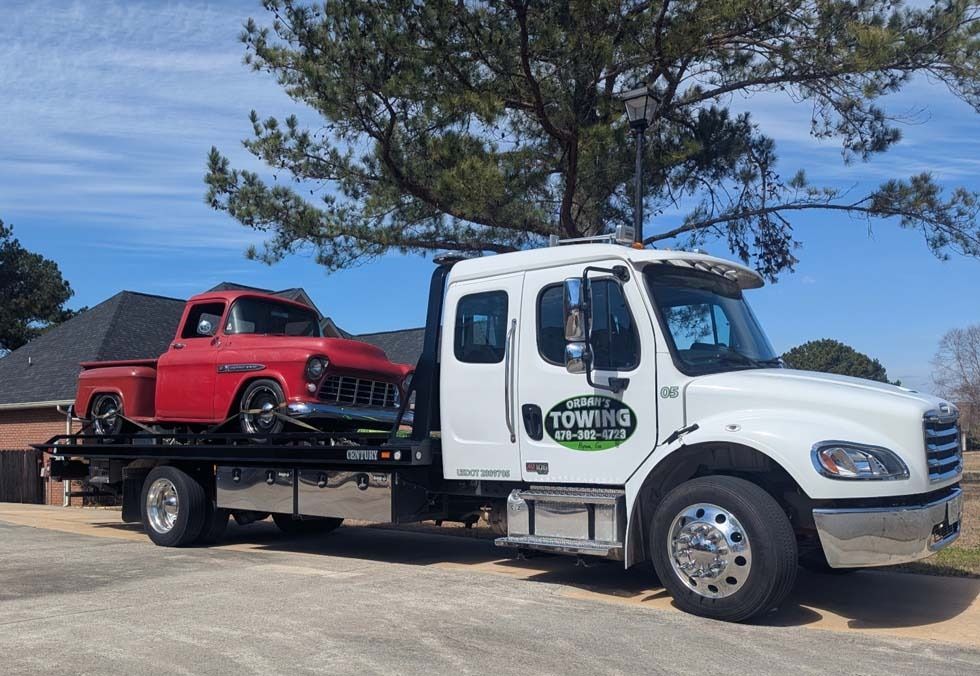 White tow truck carrying a red classic pickup truck on a sunny day.