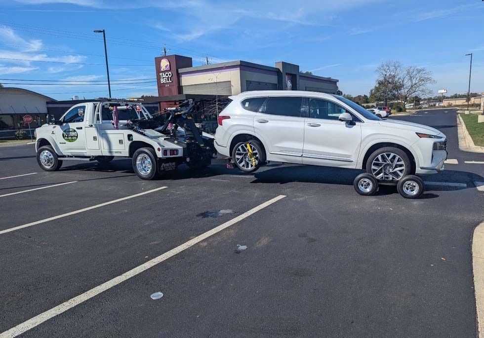 A white SUV being towed by a tow truck in a parking lot. A Taco Bell is in the background.