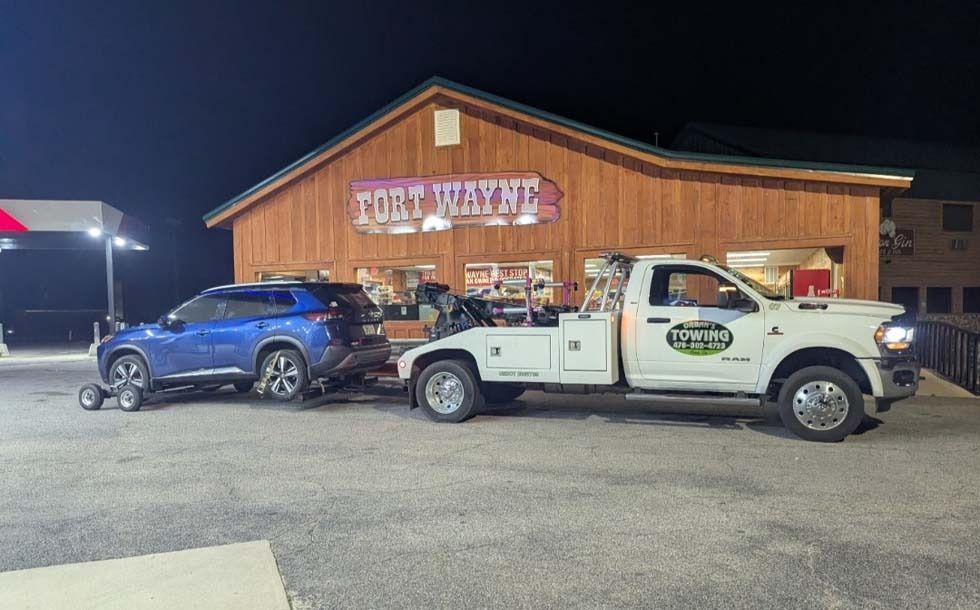 A blue SUV being towed by a white tow truck in front of a building with a 