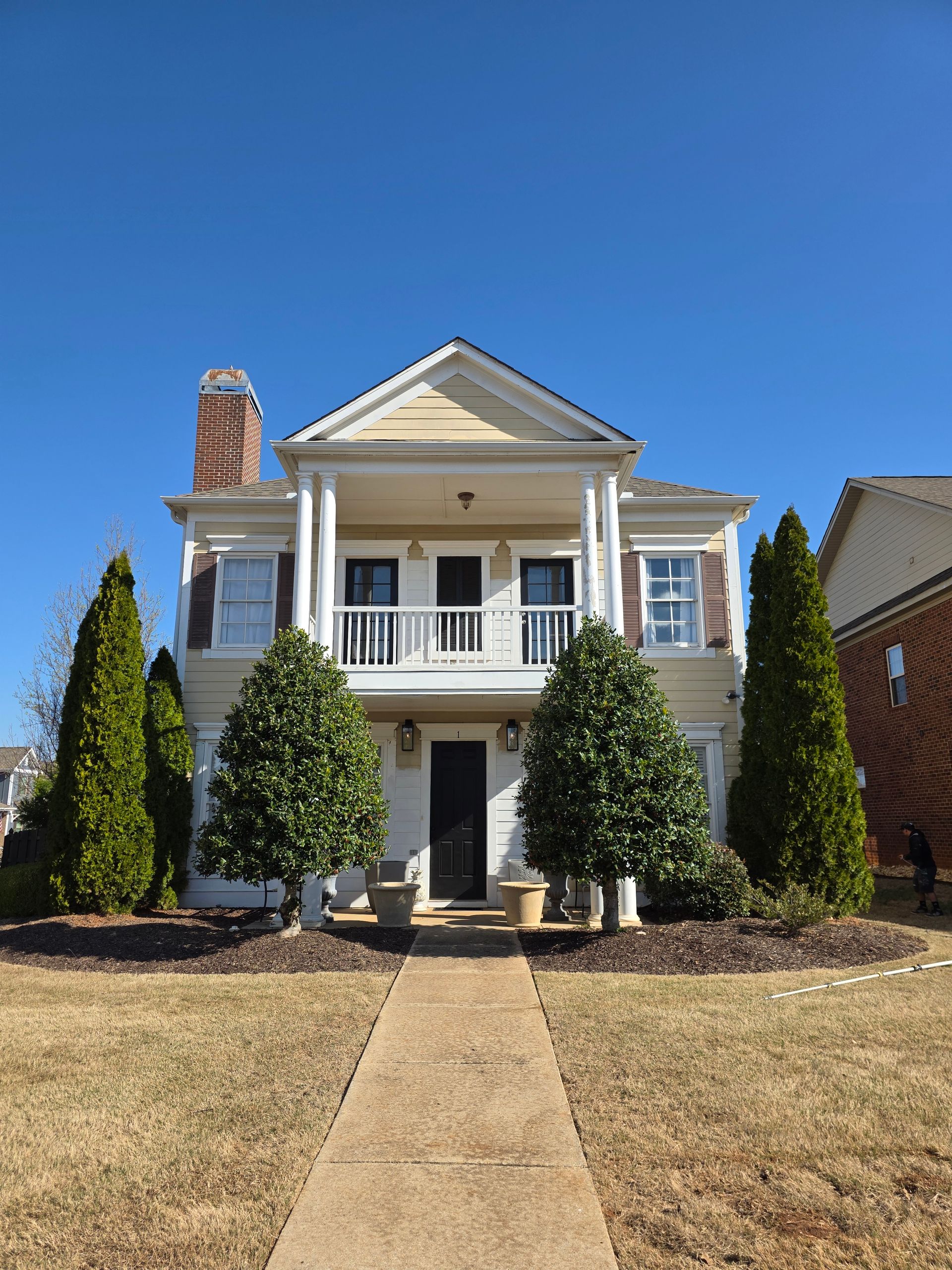 Two-story yellow house with white columns and a second-story balcony, set against a clear blue sky.