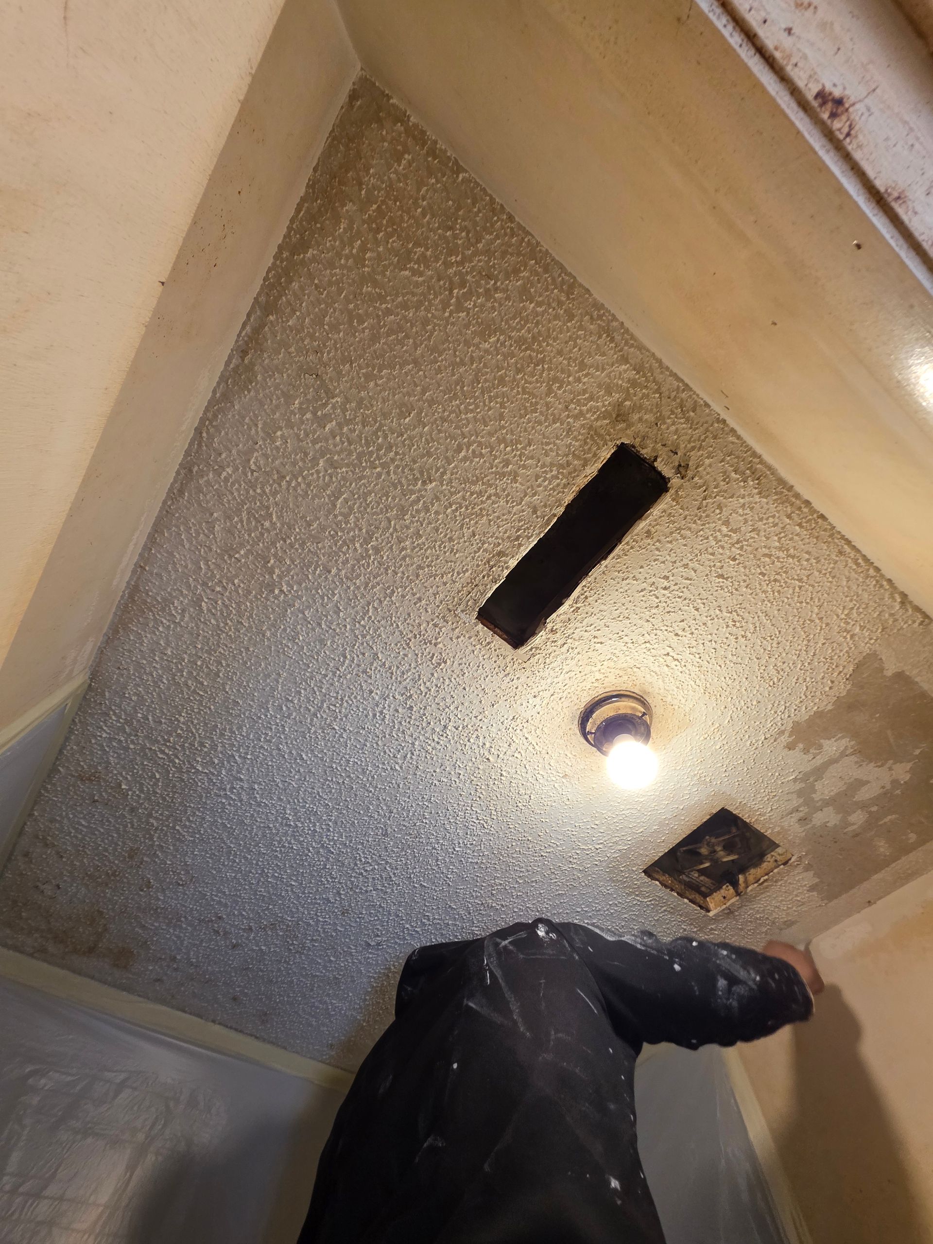 Person working on a textured, speckled ceiling with vents and a light fixture.