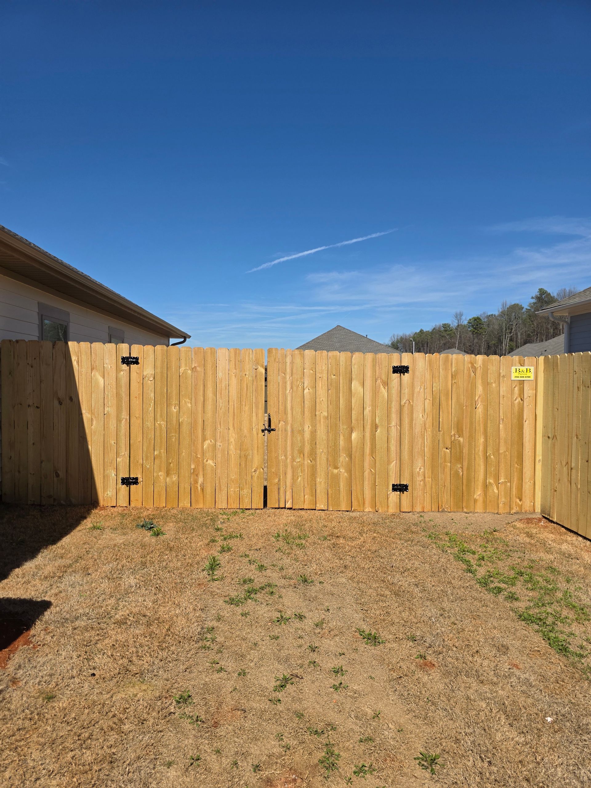 Wooden fence and gate against a blue sky, enclosing a grassy backyard.