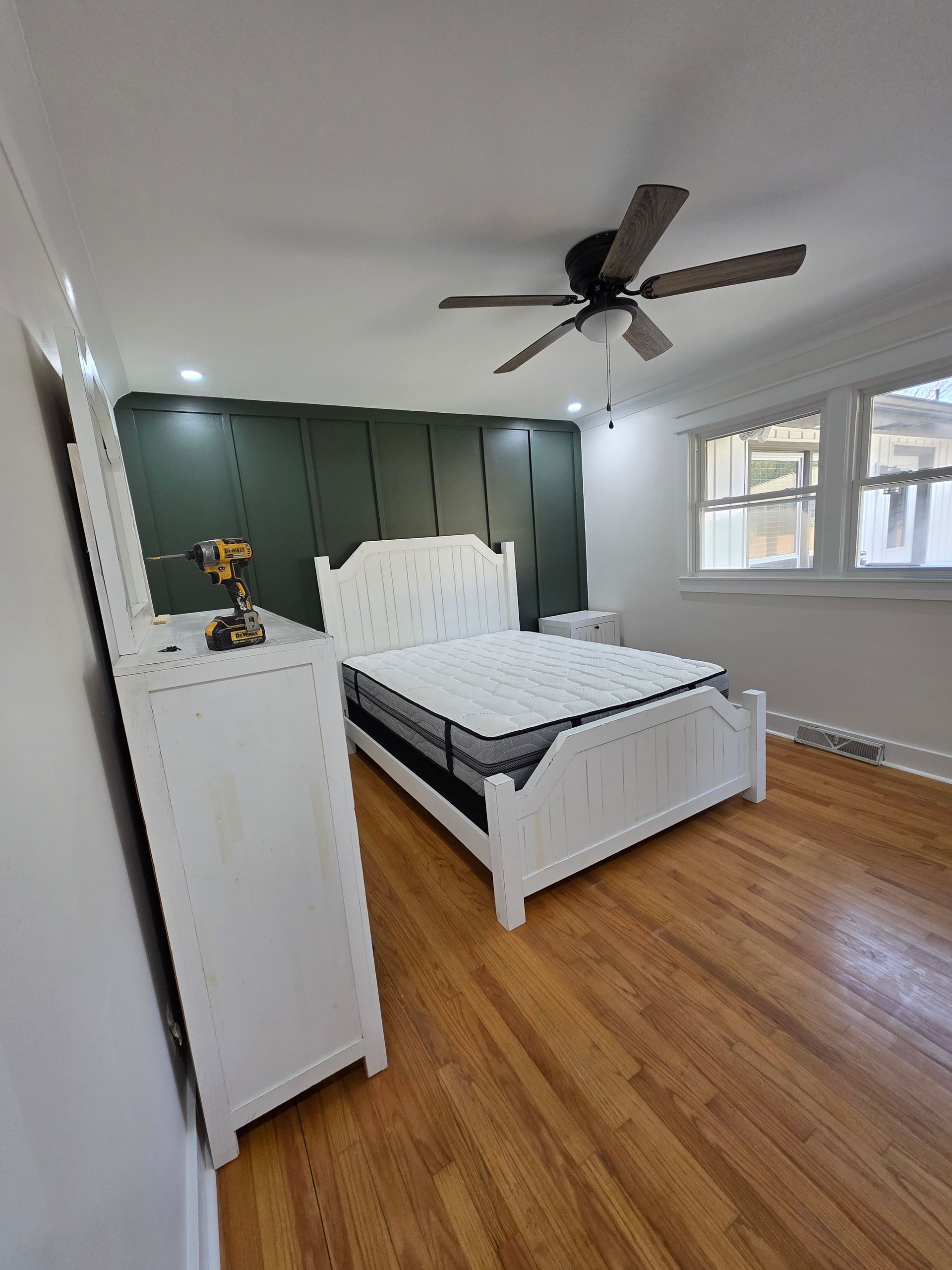 Bedroom with white furniture, wooden floors, and a green accent wall.
