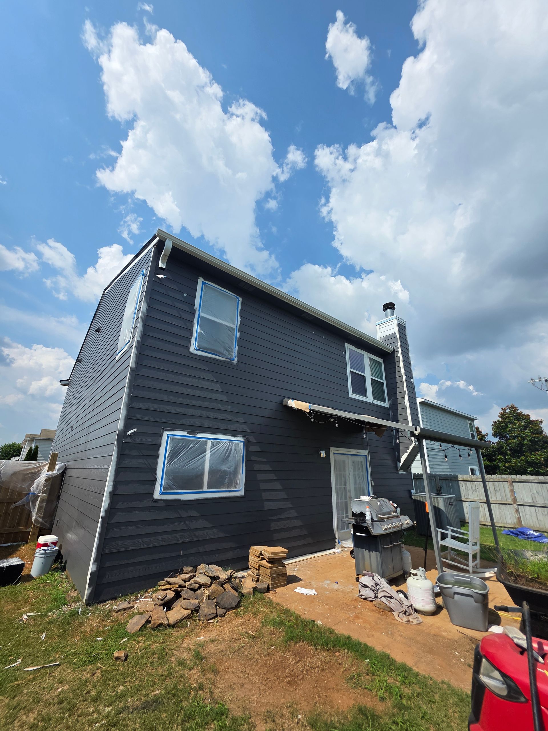 Black house exterior under construction, windows taped, blue sky with clouds.
