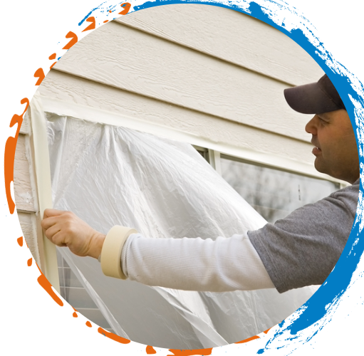 Man taping plastic sheeting to a window, preparing for painting, beige siding.