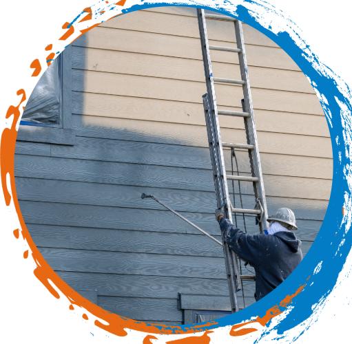 Painter spraying siding on a house from a ladder, wearing a face covering.