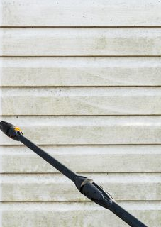 Pressure washer nozzle spraying a dirty white siding.