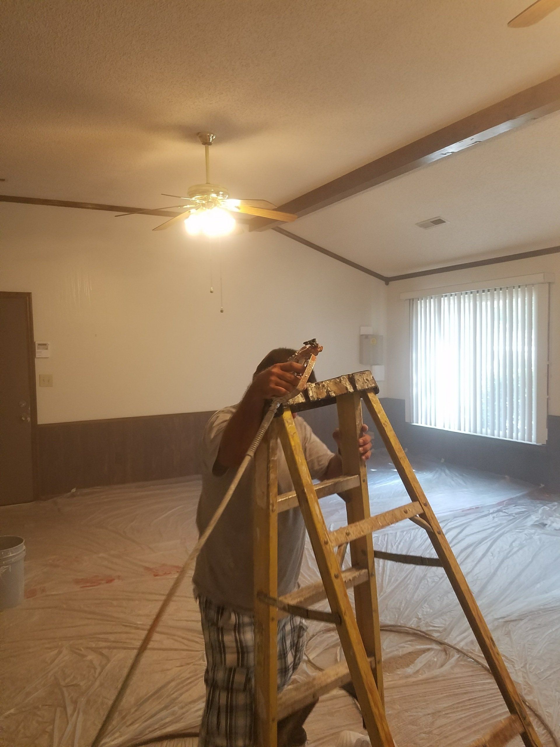 Person on ladder painting a room, walls are white and brown.