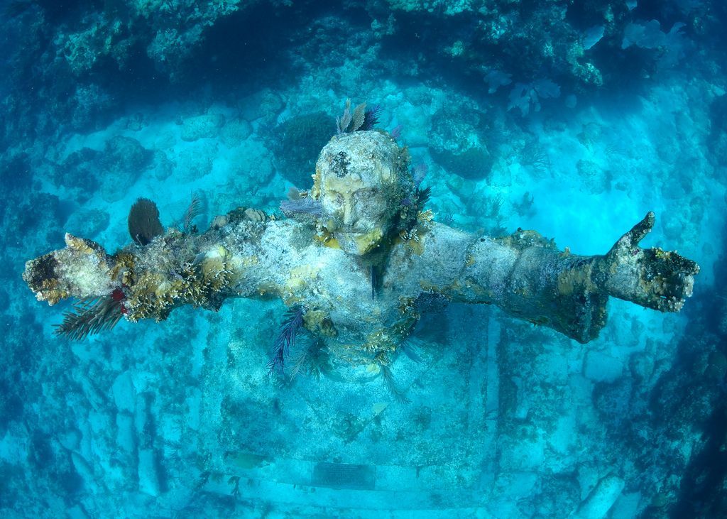 A statue of jesus is floating on top of a coral reef in the ocean.
