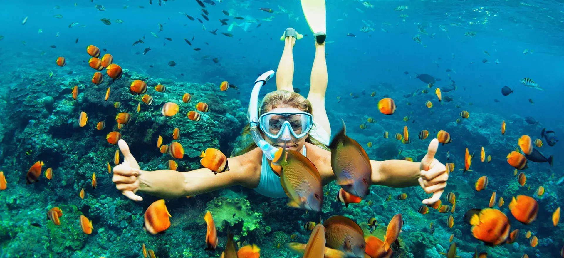 A woman is swimming in the ocean and giving a thumbs up.