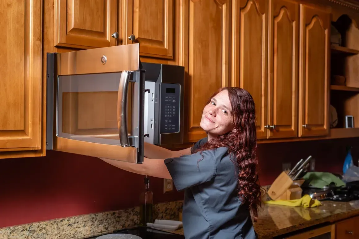 A woman is opening a microwave oven in a kitchen.