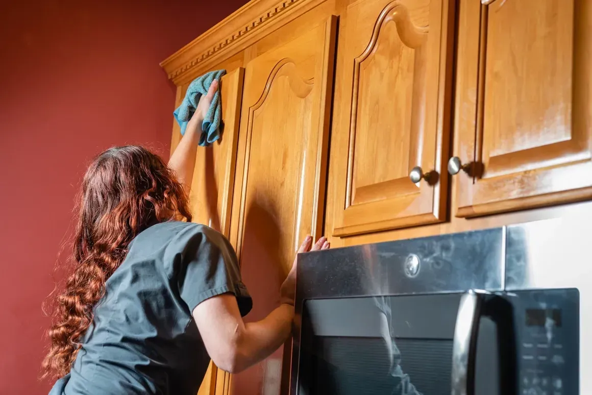 A woman is cleaning cabinets in a kitchen with a cloth.